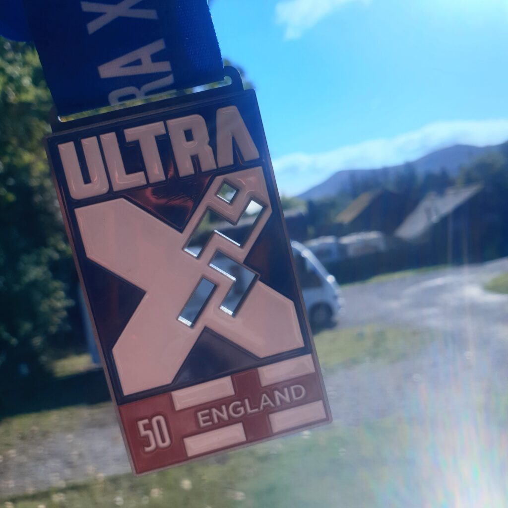 An UltraX medal for a 50k ultra running event in England with hills and a campsite in the background